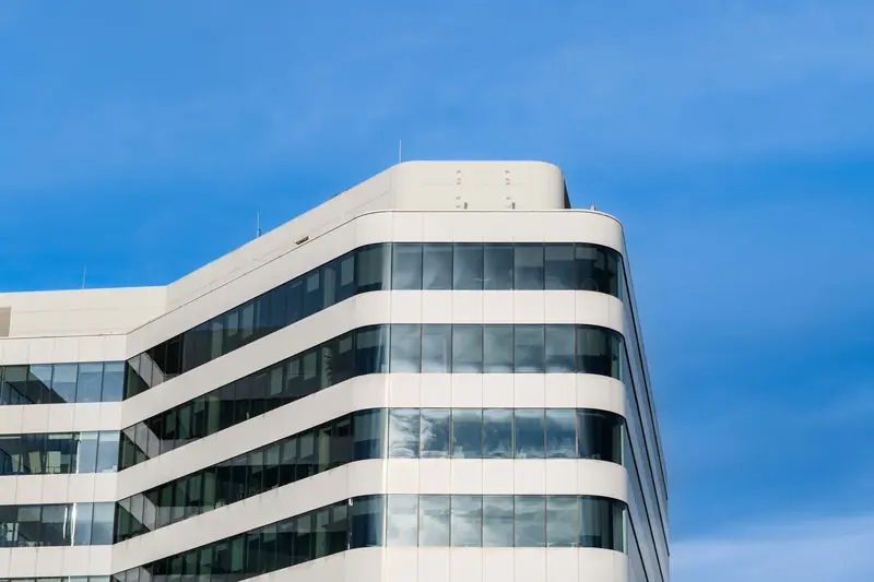 Weißes Bürogebäude mit langen Fensterbändern vor blauem Himmel