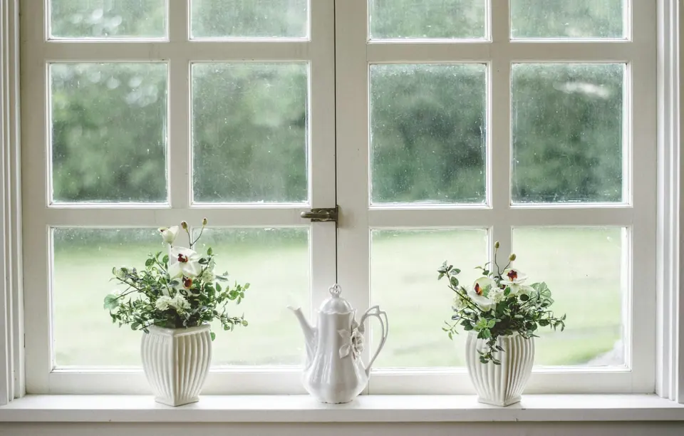 Weißes Sprossenfenster von innen mit Fensterbank, Blumen und Teekanne